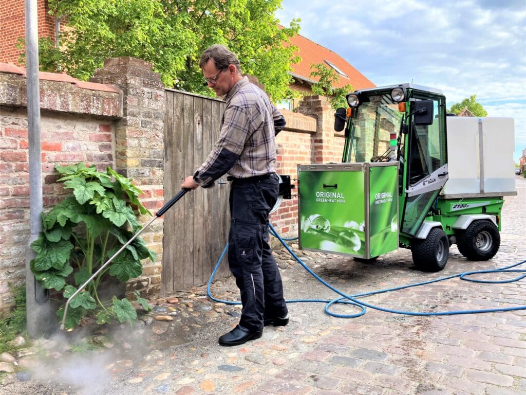Mand der udfører miljøvenlig ukrudtsbekæmpelse med 105 grader varmt vand fra en Greenheat Mini på brosten