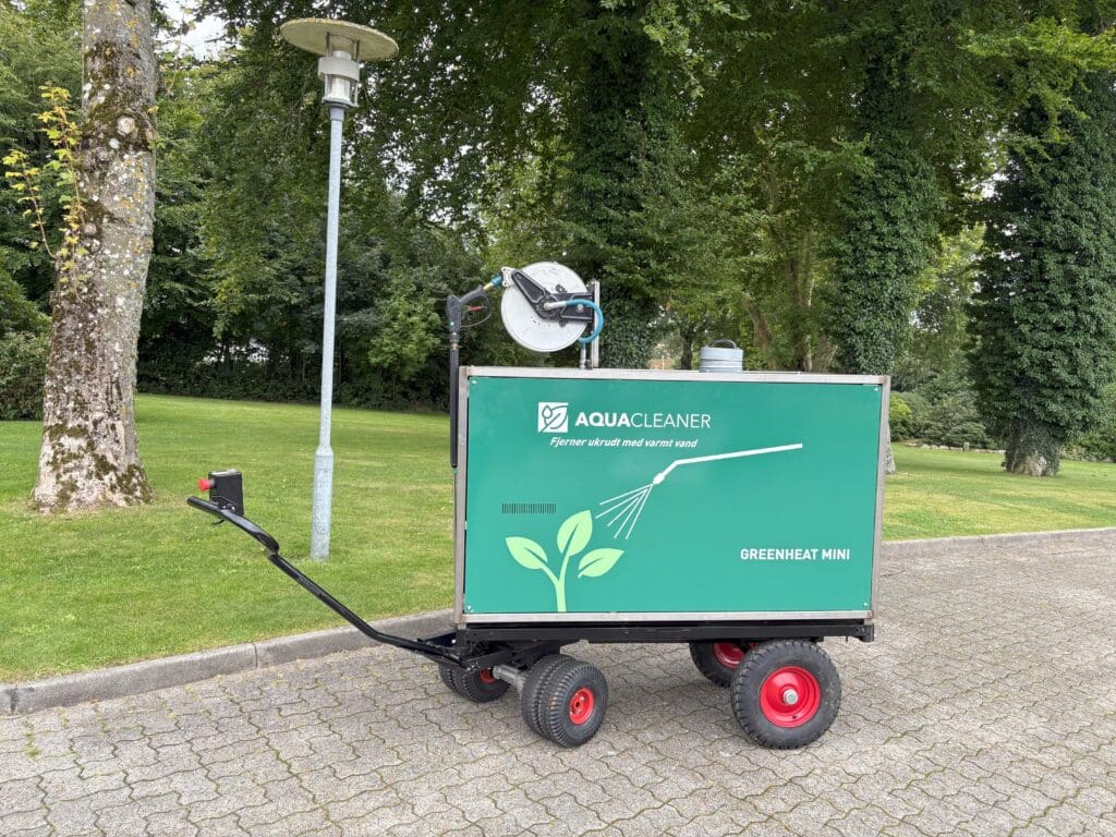 Greenheat Mini-Maschine von Aqua Cleaner für umweltfreundliche Unkrautbekämpfung mit 105 Grad heißem Wasser auf einem gepflasterten Gehweg.