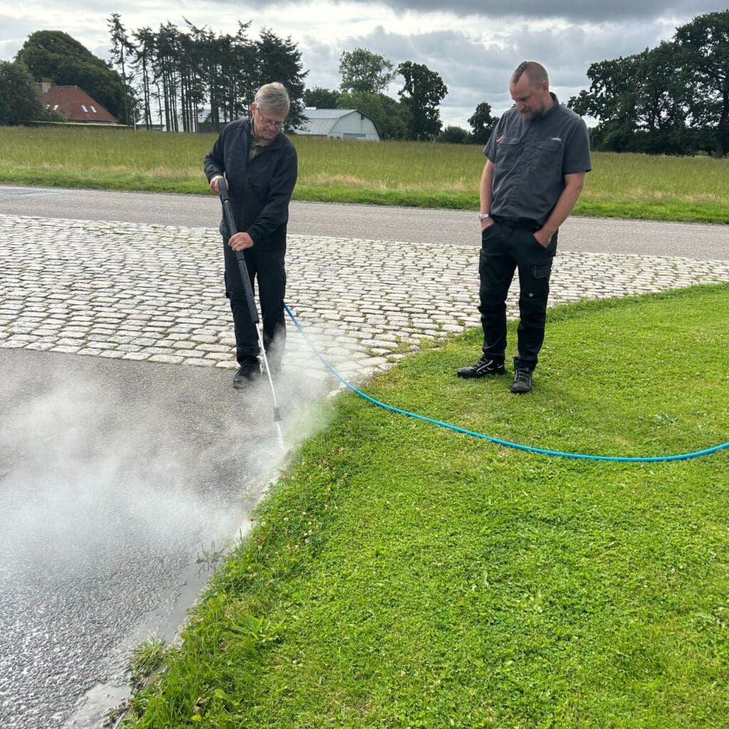 To mænd demonstrerer Greenheat Mini fra Aqua Cleaner til effektiv ukrudtsbekæmpelse med 105 grader varmt vand uden brug af kemikalier.
