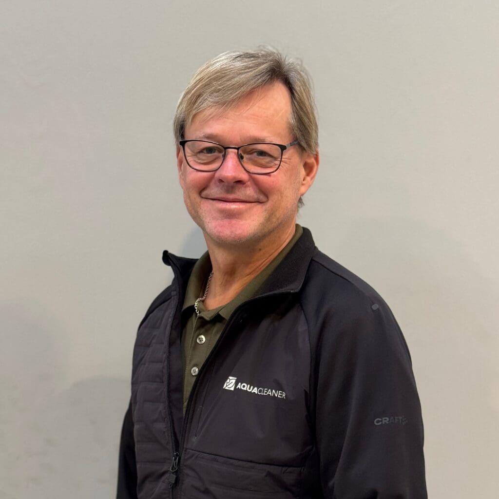 Porträt von Tom von Aqua-Cleaner, lächelnder Mann mit Brille und schwarzer Jacke mit Aqua-Cleaner-Logo, Spezialist für Hochdruckreiniger.